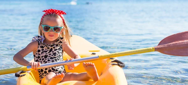 Kleines süßes Mädchen genießt das Schwimmen auf dem gelben Kajak im klaren türkisfarbenen Wasser — Stockfoto