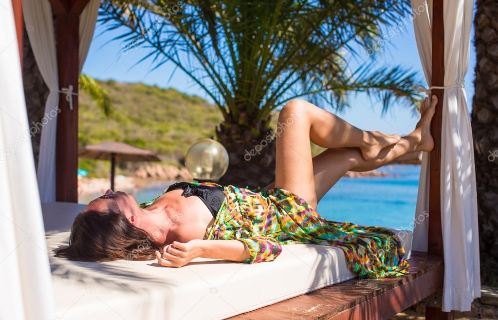 Young beautiful woman relaxing on beach bed during tropical vacation