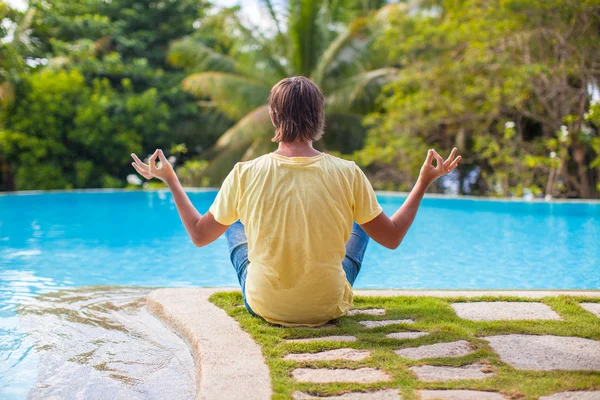 Young man sitting in lotus position near the pool — Stock Photo, Image