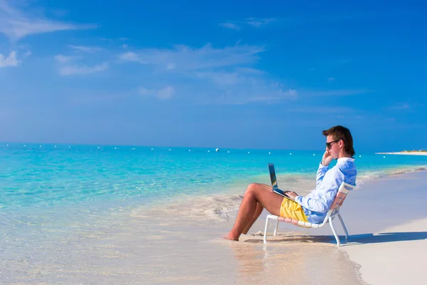 Hombre joven con portátil y teléfono celular en la playa tropical — Foto de Stock