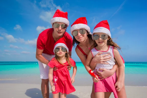 Glückliche vierköpfige Familie mit Weihnachtsmützen am weißen Strand — Stockfoto