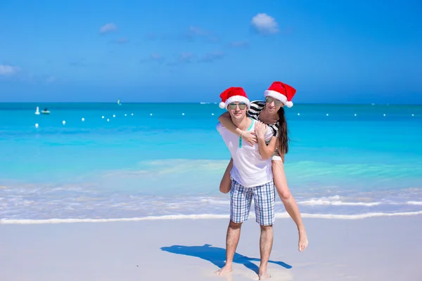 Bakifrån av par i santa hattar njuta av strandsemester — Stockfoto