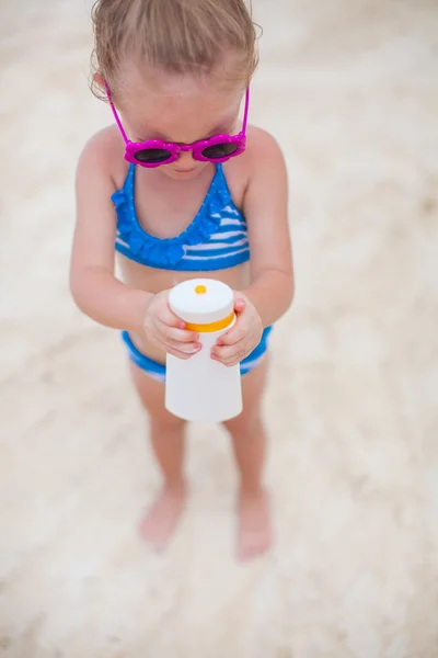 Pequeña linda adorable chica en traje de baño frota protector solar a sí misma —  Fotos de Stock
