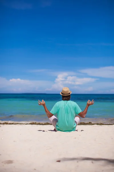 Młody człowiek siedzi w pozycji lotosu na tropikalnej plaży biały — Zdjęcie stockowe