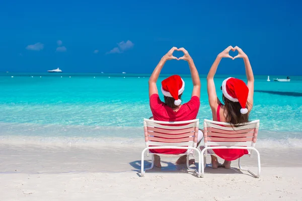 Happy romantic couple in red Santa Hats at beach making hearts — Stock Photo, Image