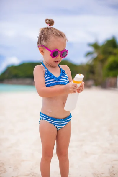 Pouco bonito adorável menina em maiô esfrega protetor solar si mesma — Fotografia de Stock