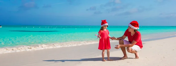 Mała dziewczynka i szczęśliwy tata w santa hat w egzotycznej plaży — Zdjęcie stockowe