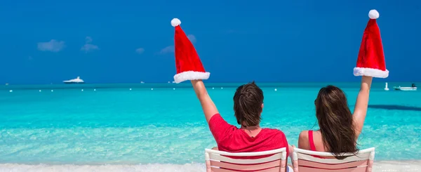 Glückliches junges Paar in roten Weihnachtsmützen auf Strandkörben sitzend — Stockfoto