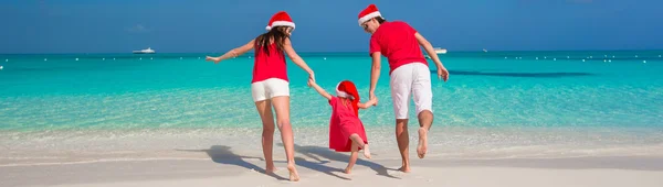 Glückliche Familie mit Weihnachtsmützen, die Spaß am weißen Strand hat — Stockfoto