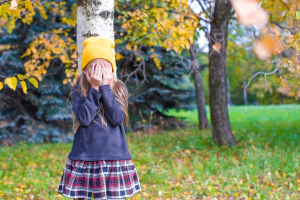 Liten flicka som leker kurragömma i höst skog — Stockfoto
