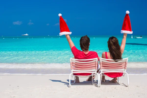Heureux jeune couple en rouge Santa Chapeaux assis sur des chaises de plage — Photo
