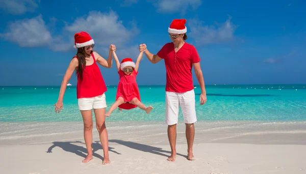 Dreiköpfige glückliche Familie mit Weihnachtsmützen amüsiert sich am weißen Strand — Stockfoto