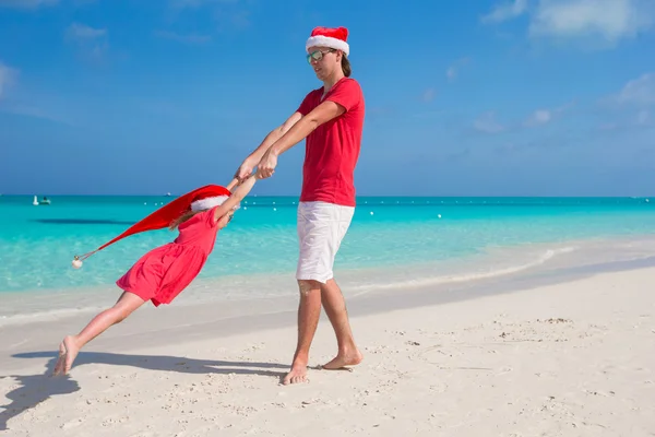 Mała dziewczynka i szczęśliwy tata w santa hat zabawy na tropikalnej plaży — Zdjęcie stockowe