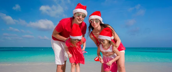 Glückliche vierköpfige Familie mit Weihnachtsmützen am weißen Strand — Stockfoto