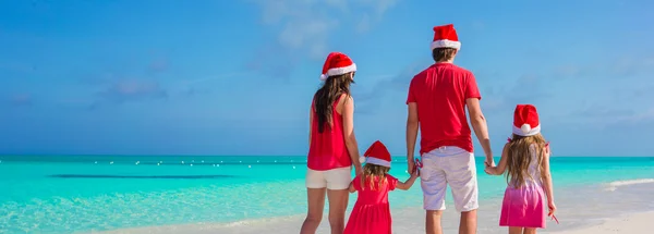 Happy family of four in Christmas Hats on white beach — Stock Photo, Image