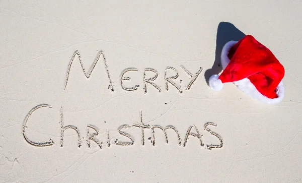 Frohe Weihnachten am tropischen Strand weißen Sand mit Weihnachtsmütze geschrieben — Stockfoto