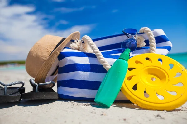 Stripe bag, straw hat, sunblock and frisbee on white sandy tropical beach — Stock Photo, Image