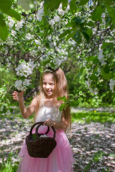 Adorable niña pequeña con cesta de paja en el jardín de manzanas en flor —  Fotos de Stock