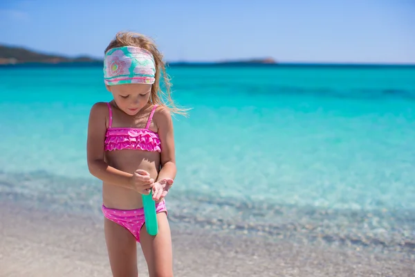 Piccola adorabile ragazza in costume da bagno con bottiglia di crema abbronzante — Foto Stock