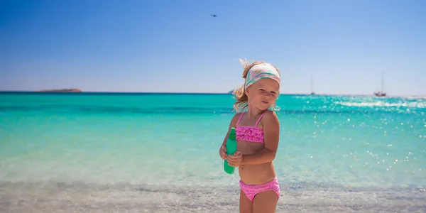 Niña adorable en traje de baño con botella de loción bronceadora —  Fotos de Stock