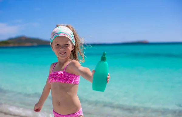 Niña adorable en traje de baño con botella de loción bronceadora —  Fotos de Stock