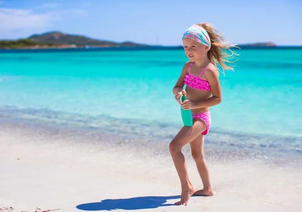 Piccola adorabile ragazza in costume da bagno con bottiglia di crema abbronzante — Foto Stock