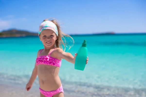 Niña adorable en traje de baño con botella de loción bronceadora —  Fotos de Stock