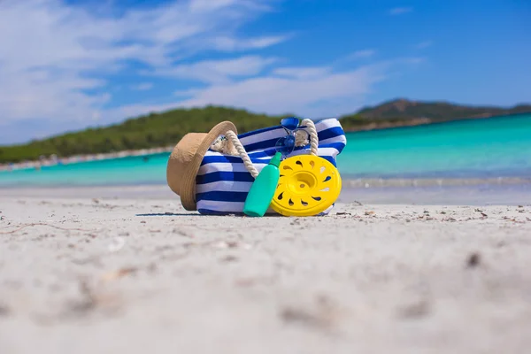 Borsa a righe, cappello di paglia, crema solare e frisbee sulla spiaggia tropicale di sabbia bianca — Foto Stock
