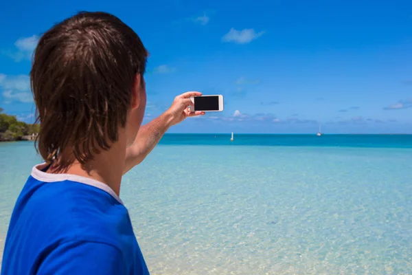 Young man in santa hat with phone on tropical caribbean beach — Stock Photo, Image