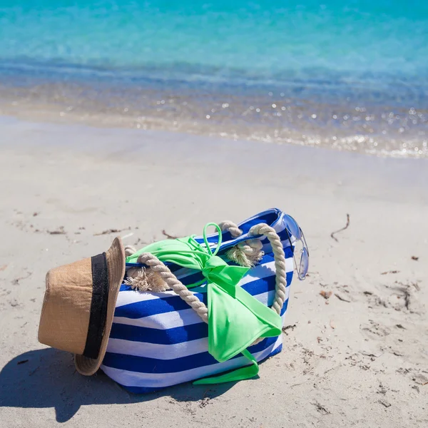 Stripe bag, straw hat, sunblock and frisbee on white sandy tropical beach — Stock Photo, Image