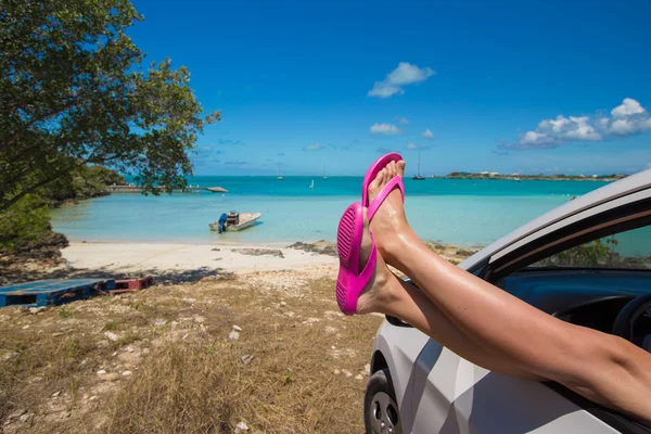 Chanclas desde la ventana de un coche en la playa tropical de fondo — Foto de Stock