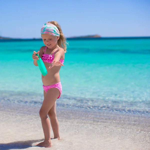 Piccola adorabile ragazza in costume da bagno con bottiglia di crema abbronzante — Foto Stock