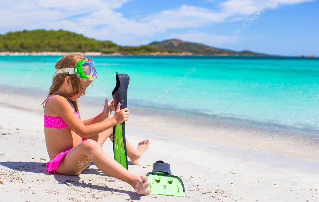 Little girl with flippers and goggles for ssnorkling on the beach