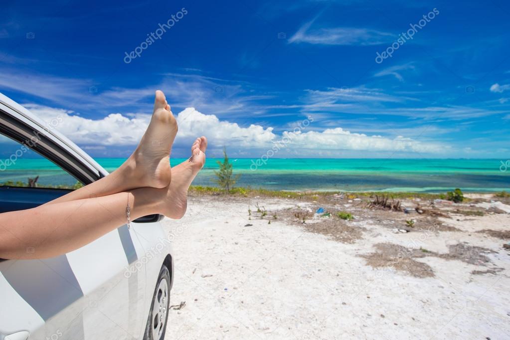 Female barefoot from the window of a car on background tropical beach