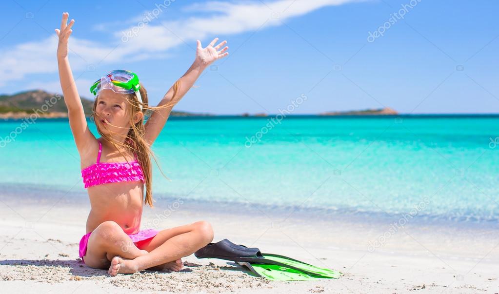 Little girl with flippers and goggles for ssnorkling on the beach