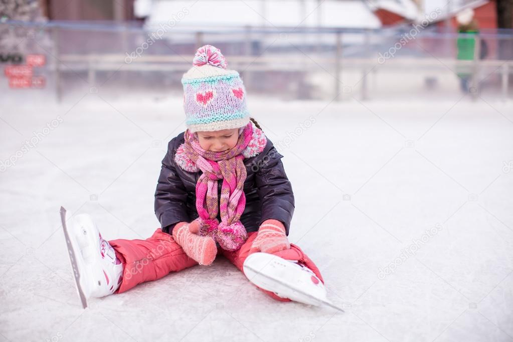 Little sad girl sitting on skating rink after the fall