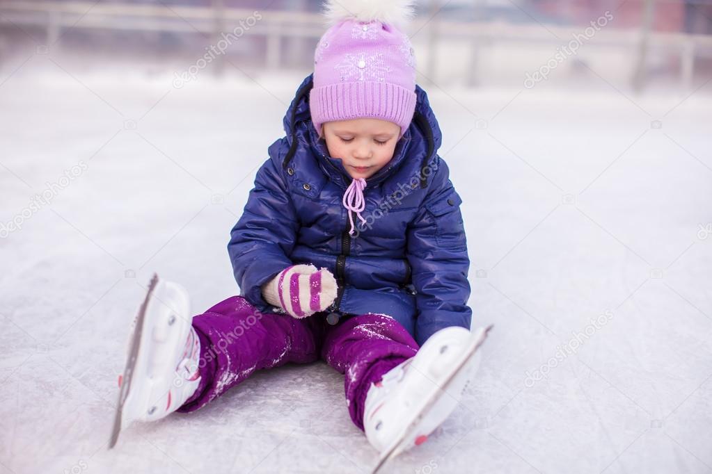 Adorable little girl sitting on ice with skates after the fall