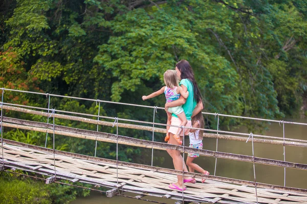 Young mother with her little girls on suspension bridge over the River — Stock Photo, Image