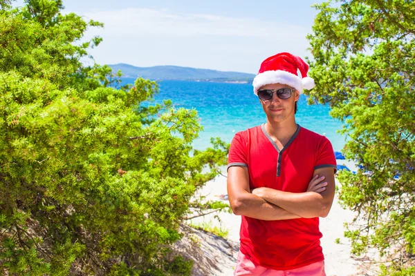 Jeune homme en rouge Chapeau de Noël sur la plage tropicale près des sapins — Photo