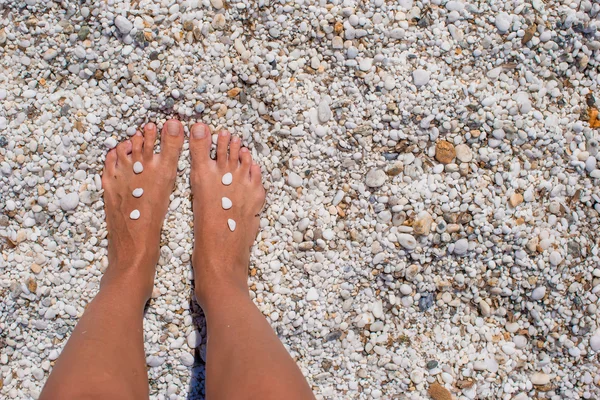 Closeup of female legs with pebbles on white sandy beach — Stock Photo, Image