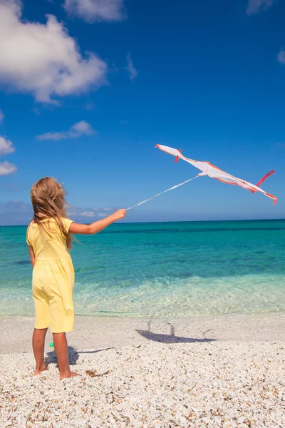 Kleines süßes Mädchen spielt mit fliegendem Drachen am tropischen Strand — Stockfoto