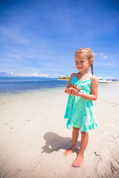 Little adorable girl with starfish in hands at the tropical beach — Stock Photo, Image