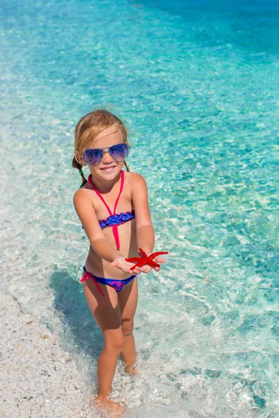 Niña adorable con estrella de mar en la playa tropical —  Fotos de Stock