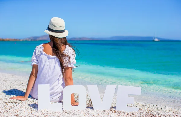 Молодая красивая женщина сидит на пляже со словом Любовь — стоковое фото