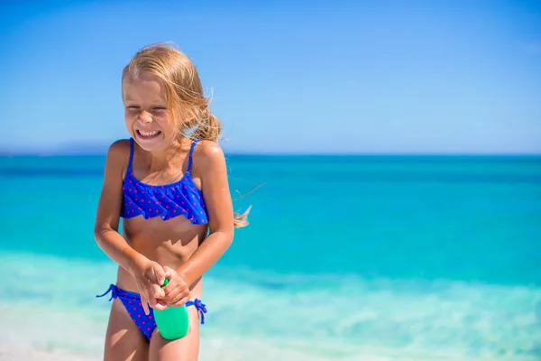 Pequena menina feliz com garrafa loção bronzeado do sol durante as férias na praia — Fotografia de Stock