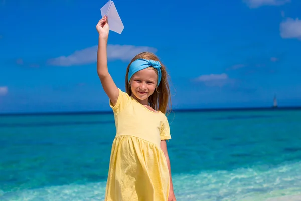 Šťastná holčička hrát s papírové letadlo na bílé písečné pláži — Stock fotografie