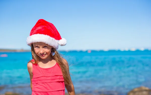 Linda niña en el sombrero de Santa en la playa durante las vacaciones —  Fotos de Stock