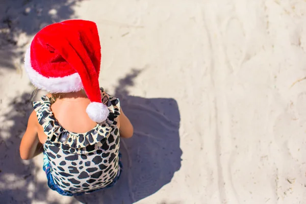 Roztomilá holčička v červeném klobouku Santa na bílé pláži venku — Stock fotografie