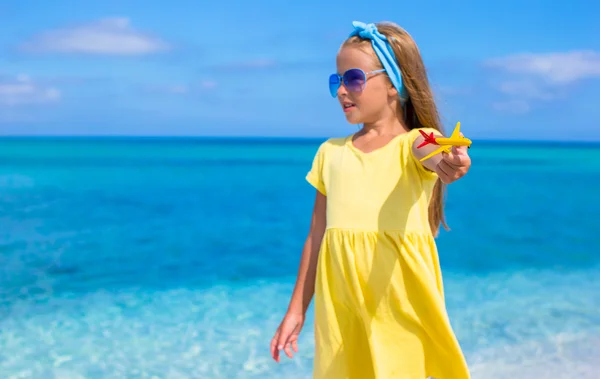 Счастливая маленькая девочка с игрушечным самолетом в руках на белом пляже — стоковое фото