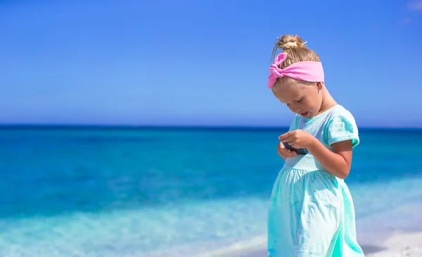 Kleines entzückendes Mädchen spielt während des Strandurlaubs im Handy — Stockfoto